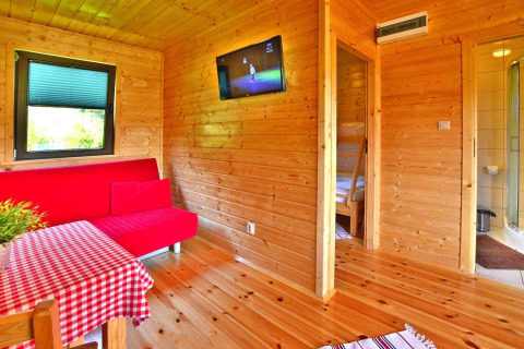 Houten chaletinterieur met rode bank, tv en eettafel in Mielno, Denemarken voor vijf personen.