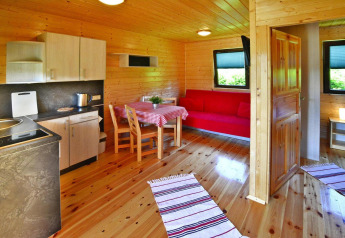 Interieur van een knusse houten blokhut met keuken, eettafel, rode bank en veel daglicht.