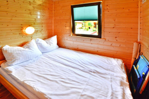 Slaapkamer in een zomerhuisje met tweepersoonsbed, houten wanden en raam voor 5 personen in Mielno.