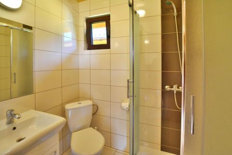 Helles Badezimmer in einer Sommerhütte bei Mielno mit Dusche, WC, Waschbecken und kleinem Fenster.