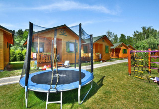 Zomerhuisjes van hout met trampoline en speeltoestellen in het gras, perfect voor gezinnen met kinderen.