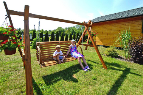 Zwei Kinder sitzen auf einer Holzschaukel im Garten der Sommerhäuser für 5 Personen in Mielno, Dänemark.