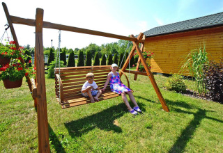 Twee kinderen zitten op een houten schommel bij zomerhuisjes voor 5 personen in Mielno, Denemarken.