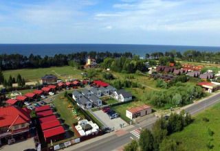 Holiday cottages in Gąski near the sea, surrounded by greenery, aerial view taken on a bright sunny day.