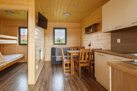Interior view of a holiday cottage in Gąski, Denmark with wooden walls, kitchen, dining area and bunk beds.