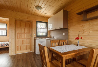 Houten interieur van een vakantiewoning met eettafel, vier stoelen, keuken en slaapkamer op de achtergrond.