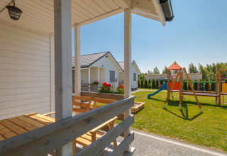 Zicht vanaf het terras bij de vakantiehuisjes in Gąski, Denemarken, met speeltuin en zonnig grasveld.