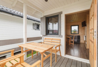 Covered terrace with wooden furniture at a holiday cottage in Gąski, view into cozy living area.