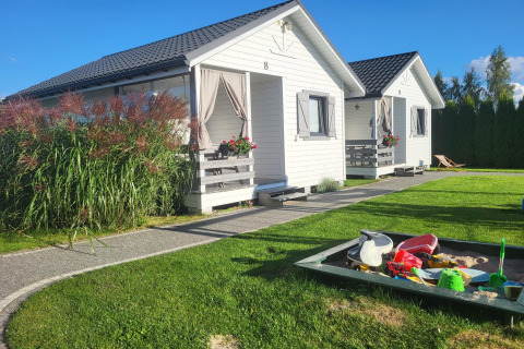 White holiday cottages in Gąski, Denmark, with a sandbox and garden, under a bright blue sky.