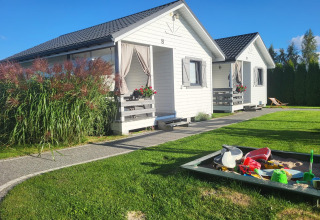 Witte vakantiehuisjes in Gąski, Denemarken, met zandbak en groene tuin onder een blauwe hemel.