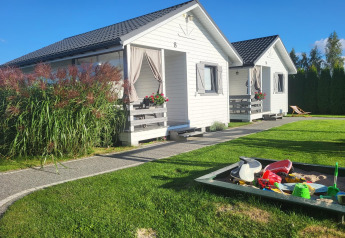 White holiday cottages in Gąski, Denmark, with a sandbox and garden, under a bright blue sky.