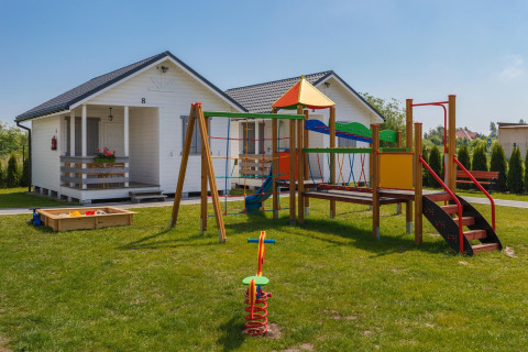 Playground with swings and colorful equipment near white holiday cottages in Gąski, Denmark, on a sunny day.