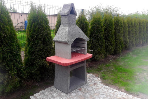 Betonnen tuinbarbecue met rood werkblad bij vakantiehuisjes in Gąski, Denemarken naast een haag.