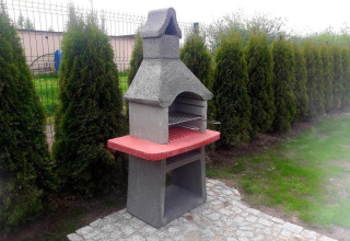 Betonnen tuinbarbecue met rood werkblad bij vakantiehuisjes in Gąski, Denemarken naast een haag.