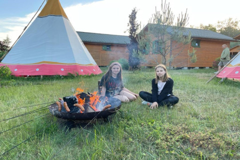Twee meisjes zitten bij een kampvuur en roosteren worsten naast tipi’s en zomerhuisjes in Mielno, Denemarken.