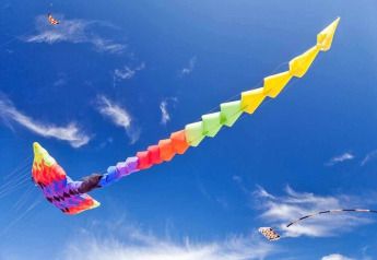 A colorful kite soars high in a clear blue sky with clouds, pictured during a visit to a cabin.