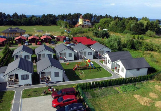 Luchtfoto van vakantiehuisjes in Gąski, Denemarken, met witte huisjes, speeltuin en geparkeerde auto's.