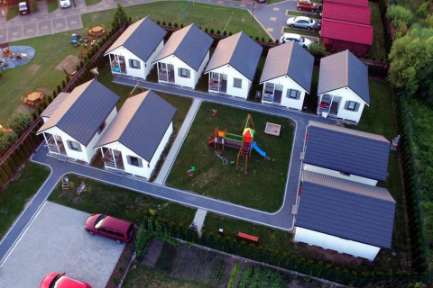 Luchtbeeld van vakantiehuisjes in Gąski met een speeltuin centraal, groene gazons en geparkeerde auto's.