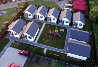Luchtbeeld van vakantiehuisjes in Gąski met een speeltuin centraal, groene gazons en geparkeerde auto's.