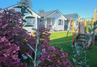 Ferienhäuser in Gąski mit blühenden Sträuchern im Vordergrund und Spielplatz auf einer grünen Wiese.