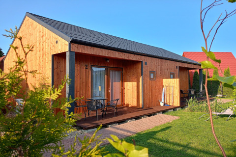 Sunny day at Twin single-storey cottages Jarosławiec with wooden lodge, patio furniture, and green lawn.