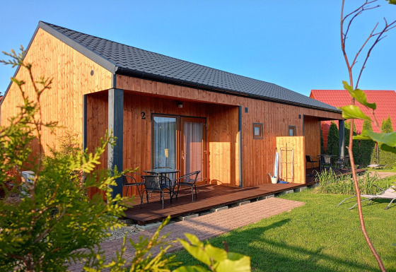 En solrig dag ved Twin single-storey cottages Jarosławiec, hvor træhytter og grønne plæner dominerer.