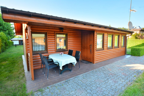 Houten chalet met terras, buitentafel en stoelen, tuin bij House in Rosnowo op een zonnige dag.