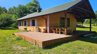 Gezellig houten lodge met overdekt terras en tuinmeubelen in een zonnige open plek tussen de bomen.