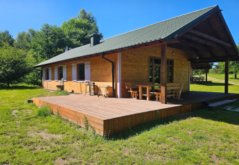 Acogedora cabaña de madera con terraza cubierta y muebles de exterior en un claro soleado rodeado de árboles.