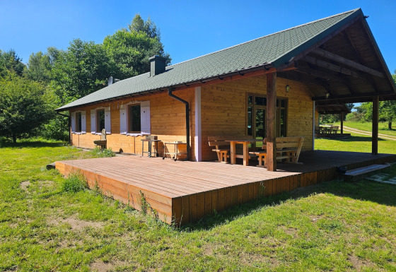 Knus houten huisje met overdekt terras en tuinmeubilair in een zonnige open plek omringd door bomen.