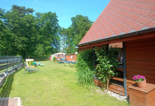 Sunny garden at Twin single-storey cottages Jarosławiec, Denmark, with loungers, playground, and red lodge.