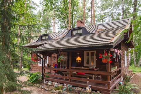 Charmante maison de vacances en bois dans une forêt verdoyante avec terrasse couverte et fleurs suspendues.