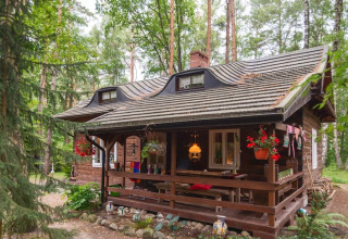 Charmante maison de vacances en bois dans une forêt verdoyante avec terrasse couverte et fleurs suspendues.