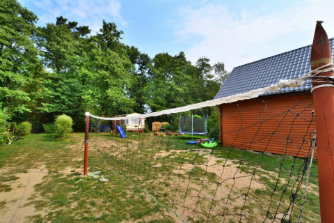 Buitenspeelplaats bij een lodge met schommel, glijbaan, trampoline en volleybalnet op het grasveld.