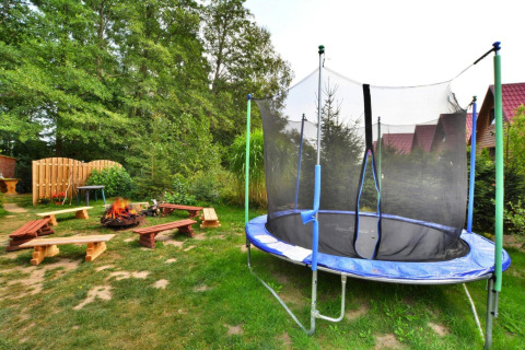 Buitenruimte bij Twin single-storey cottages Jarosławiec in Denemarken met een trampoline, vuurplaats en houten banken.