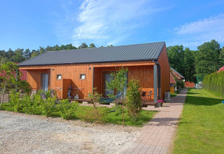 Enkelte træbygninger med sort tag, grøn græsplæne og have ved Twin single-storey cottages Jarosławiec i Danmark.