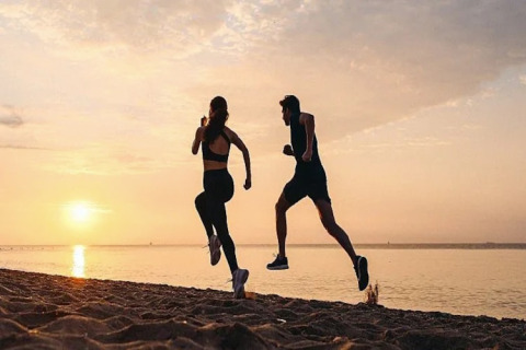 Twee mensen joggen op het strand bij zonsondergang, genieten van een actieve vakantie op een glamping.