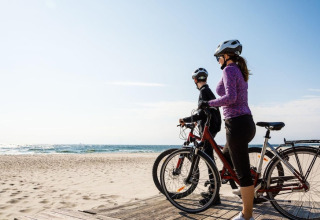 Twee mensen met fietsen genieten van het strandzicht onder een heldere lucht, sfeer van glamping.