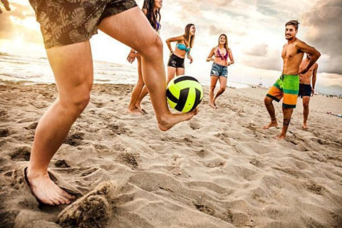 Een groep vrienden speelt op blote voeten met een bal op het strand tijdens een glampingvakantie.