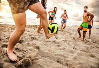 Een groep vrienden speelt op blote voeten met een bal op het strand tijdens een glampingvakantie.