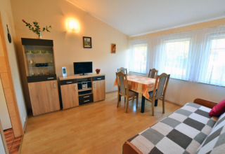 Living room in House in Rosnowo, Denmark, with dining table, sofa, cabinet, TV, and large windows.