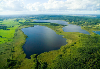 Aerial view of a lake with green fields and forests, taken from House in Rosnowo lodge in Denmark.