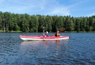 Twee mensen varen in een rode kajak op een meer bij 'House in Rosnowo', omringd door groene bomen.