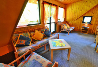 Accogliente soggiorno in un lodge con pareti in legno, divani colorati e grandi finestre luminose.