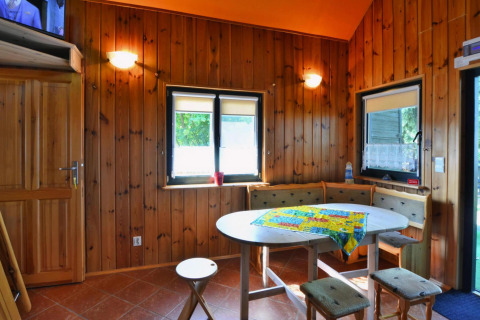 Houten lodge-interieur met knusse eethoek, ronde tafel, hoekbank en ramen met veel daglicht.