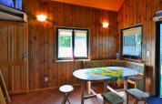 Sfeervolle eetruimte in houten chalet met ronde tafel, hoekbank en ramen met binnenvallend licht.