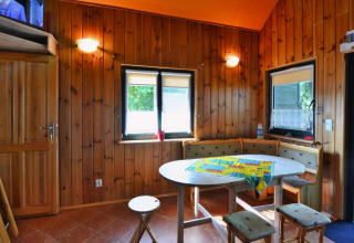 Sfeervolle eetruimte in houten chalet met ronde tafel, hoekbank en ramen met binnenvallend licht.