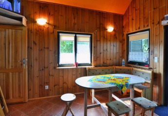 Houten lodge-interieur met knusse eethoek, ronde tafel, hoekbank en ramen met veel daglicht.