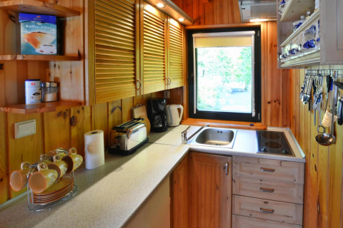 Compacte houten lodgekeuken met raam, kastjes, koffiezetapparaat, broodrooster en keukengerei op rij.