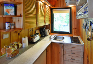 Petite cuisine de lodge en bois avec fenêtre, placards, cafetière, grille-pain et ustensiles bien rangés.